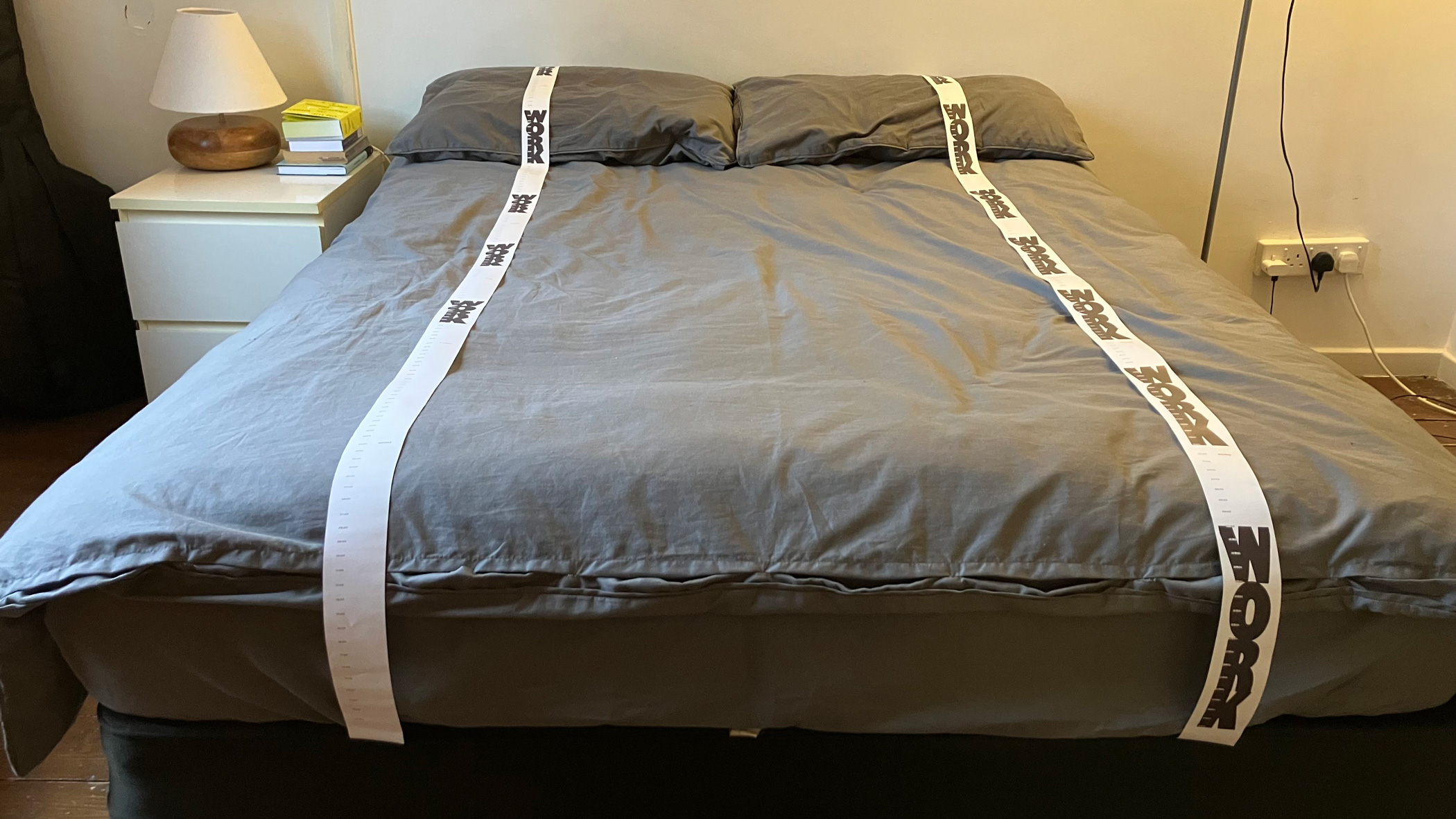 Photo of a bed with two very long receipt prints on each side. The word work is repeated on both receipts.